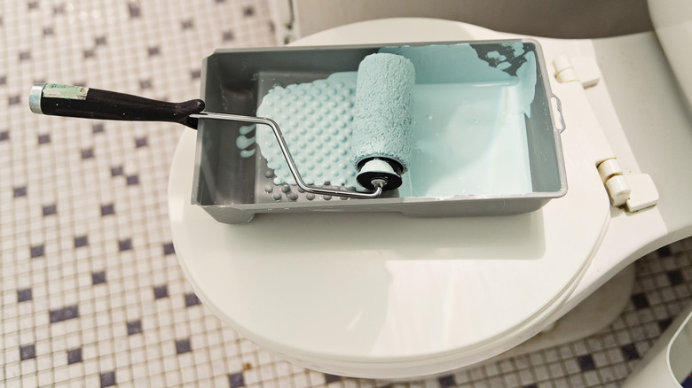 Pan of blue paint atop toilet in bathroom