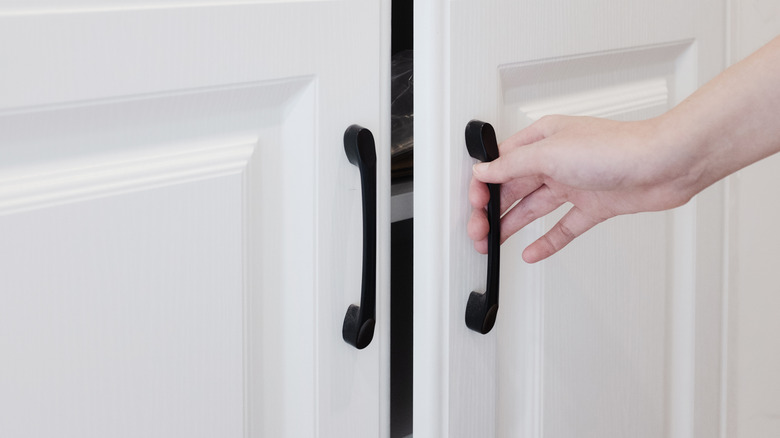 A person's hand is opening up the bar pulls on a cabinet