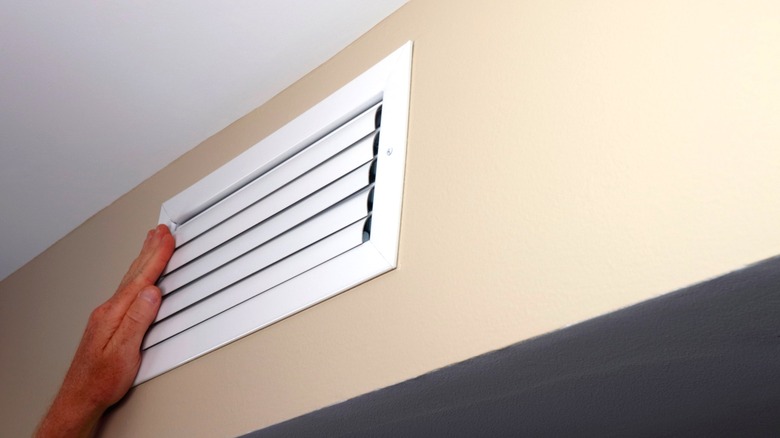 Person's hand partially covering HVAC air vent near the ceiling