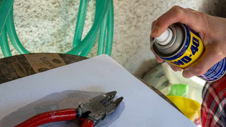 Person spraying WD-40 on pliers