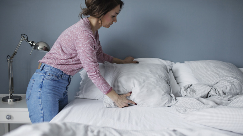 woman fluffing pillows on bed