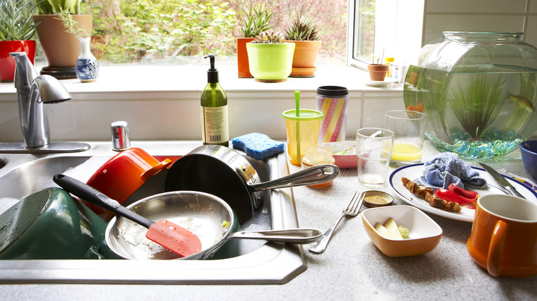 A sink full of dirty dishes set into a cluttered kitchen bench.