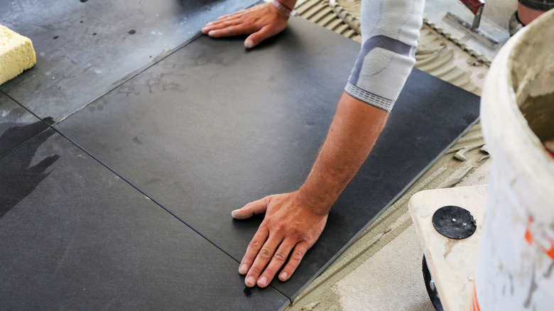 person installing square black tiles