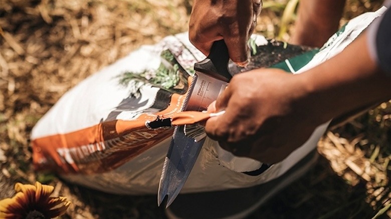 Man using a garden knife to cut open a sack