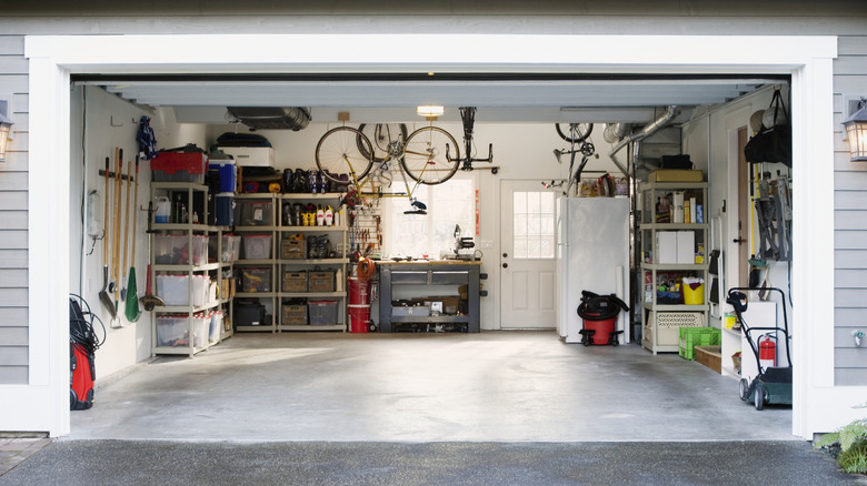 A house's garage door is open, revealing a cluttered space with tools, a bike, and a vacuum cleaner