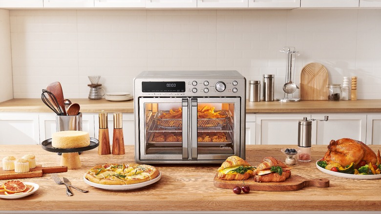 A table with the Midea Flexify French Door Air Fryer Oven, a chopping board with croissants and several plates