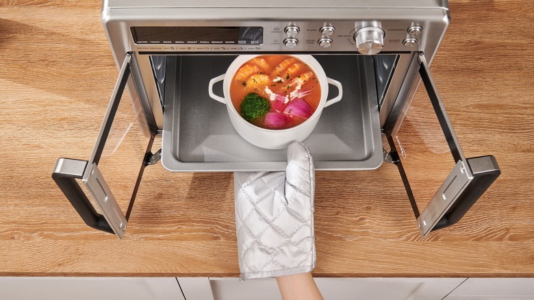 A person placing a bowl of stew in the Midea Flexify French Door Air Fryer Oven