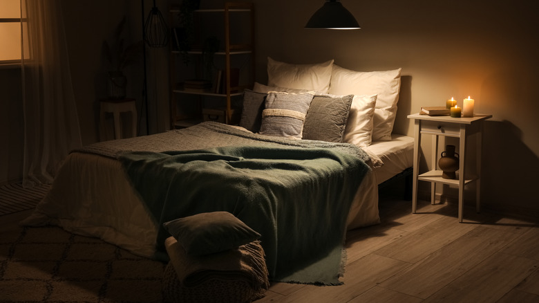 Dark bedroom with spotlight on bed and lit candles