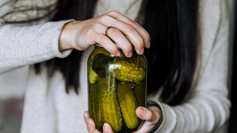 A person struggles to open a pickle jar