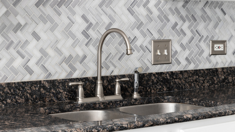 A sink with granite countertop and grey tiles