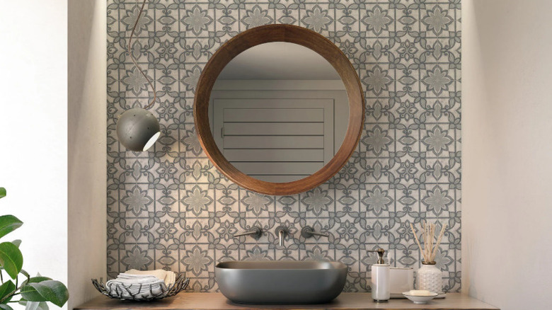 Artisanal gray-blue tiles in a bathroom are used as an accent wall with round mirror and vessel sink