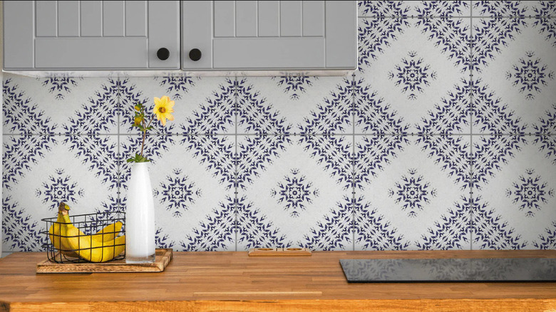 Recycled black and white tiles are used on a kitchen backsplash behind a wood countertop and induction range