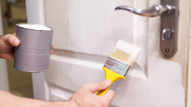 A hand painting a door with a brush