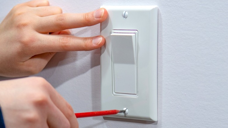 Person holding and screwing in light switch plate