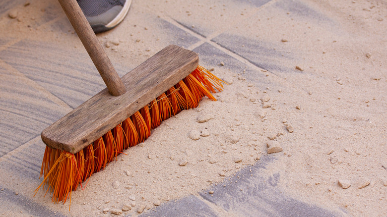 Person sweeping sand into gaps between pavers