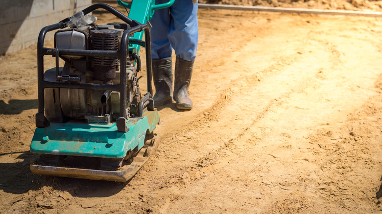 Person using a plate compactor over the top of dirt