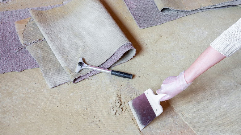 Person scrapping off carpet glue from floor