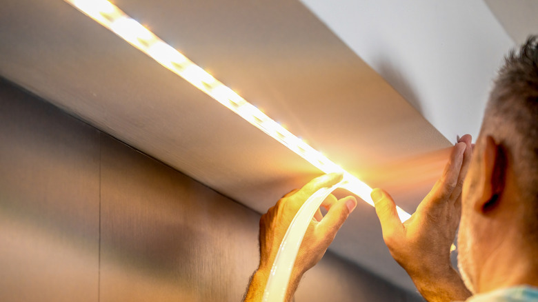 A person is installing LED strip lights under a cabinet