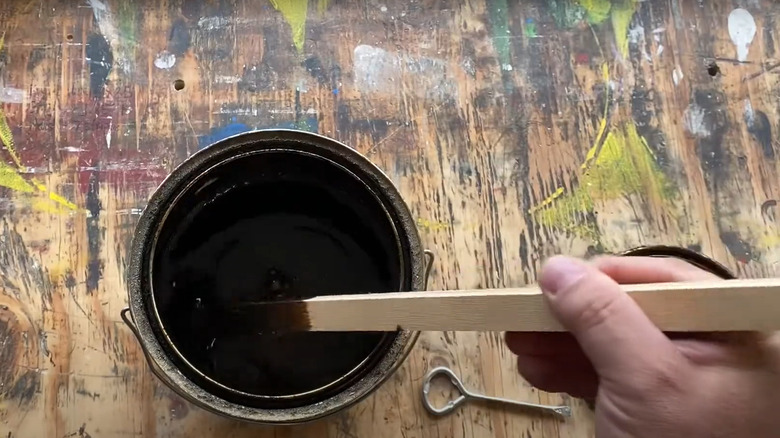 hand stirring dark wood stain with stir stick