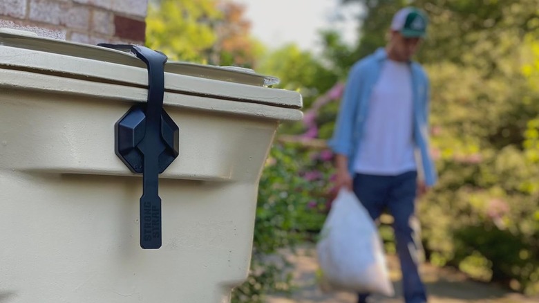 A man carrying trash to a locked trash can