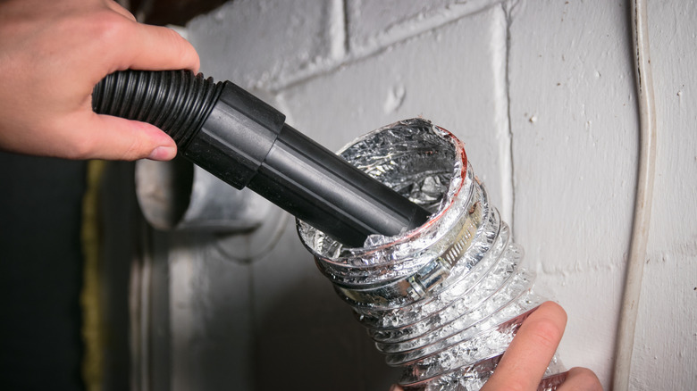 A person vacuuming inside the dryer vent