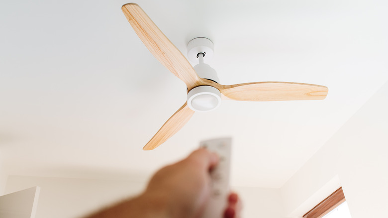 A person pointing a remote at a ceiling fan