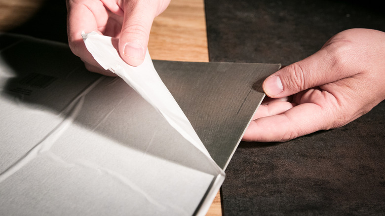 Person removing backing from a black peel-and-stick tile