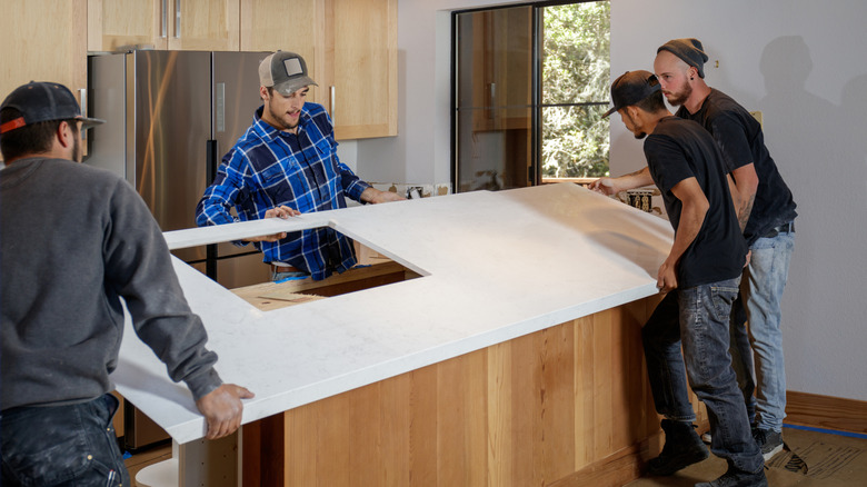 Four workers installing white kitchen counterops on an island