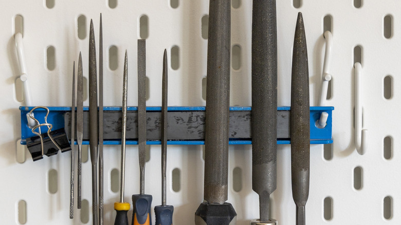 Different file tools on a magnetic strip above a work bench.