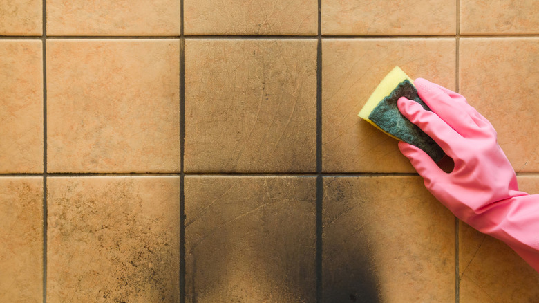 A person in pink rubber gloves using a sponge to remove soot from a tile wall