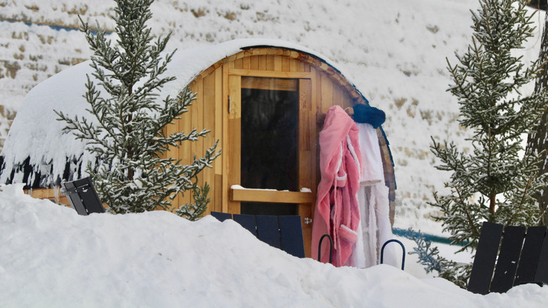 Two bathrobes hang outside a snow covered outdoor sauna