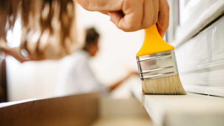 A close-up of a paint brush painting a cabinet above an open drawer