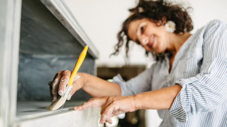 A woman painting a wooden shelf