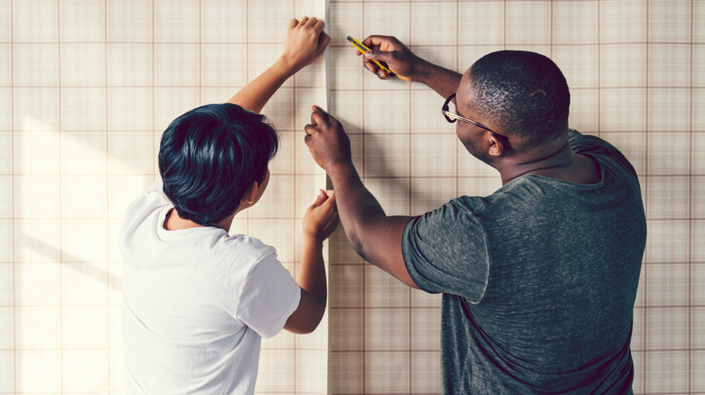 Two people putting up wallpaper