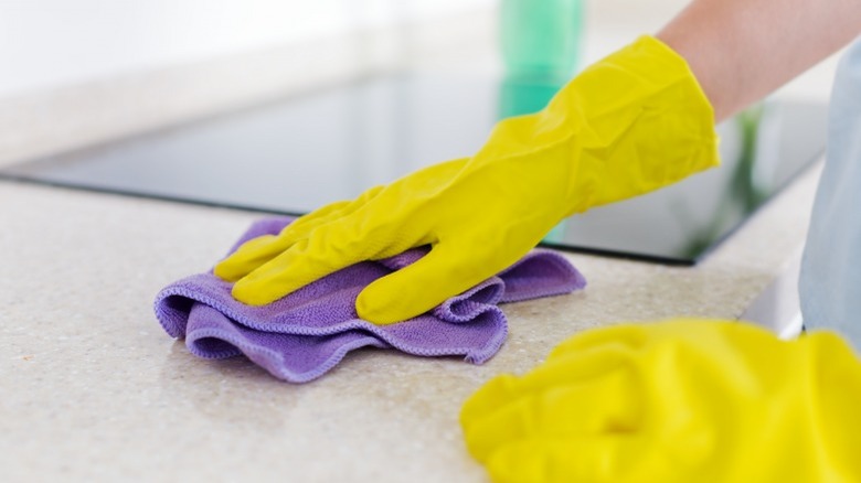 Yellow gloved hands, purple cloth cleaning white kitchen counter