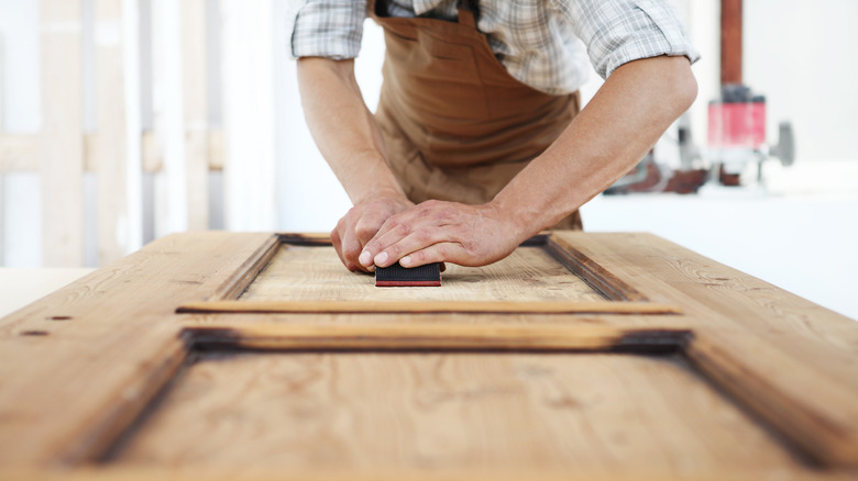 Man sanding wooded door in shop