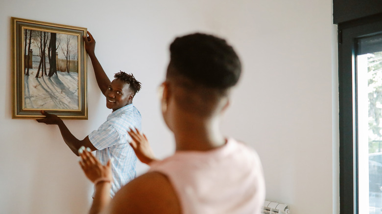 Couple hanging painting on wall