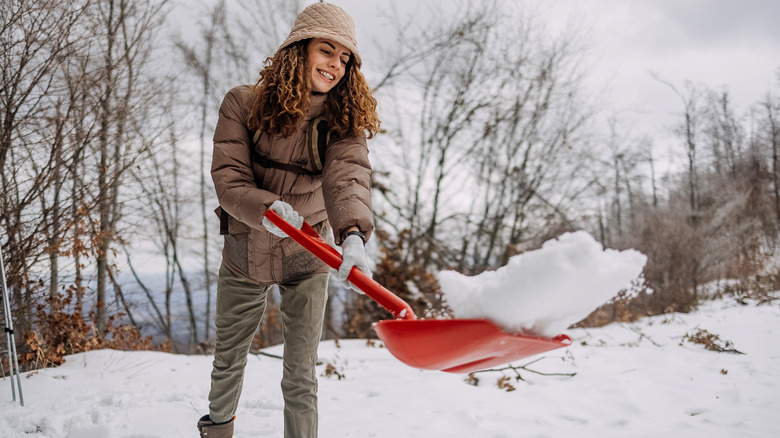 woman shoveling snow by trees
