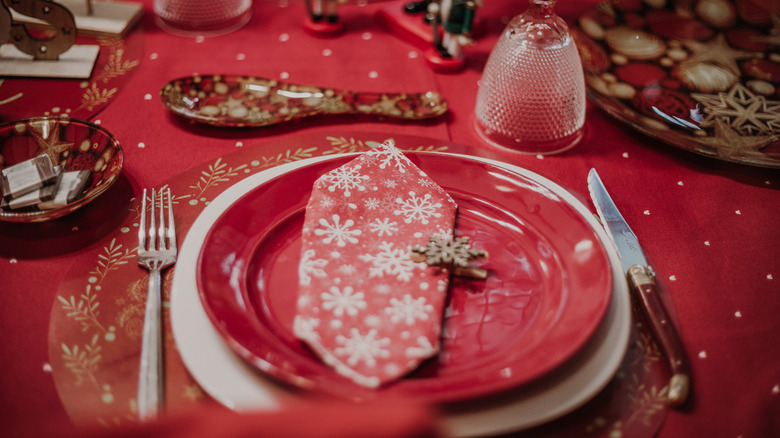 A dining table features red, white, and gold place settings.