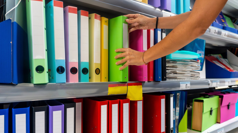 A shopper is pulling a binder from a shelf stocked with colorful binders.