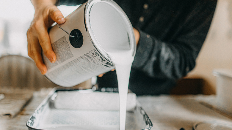 man pouring white paint can into roller tray