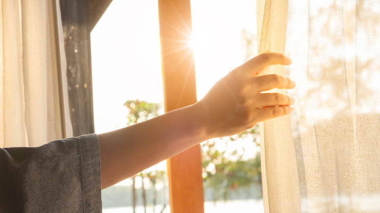 Hand pulling back curtains at a sunny window