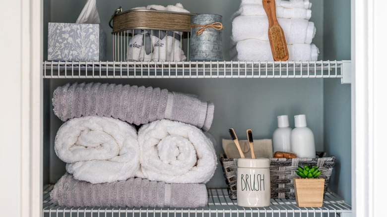 A linen closet with two wire racks with towels and toiletries stored on them