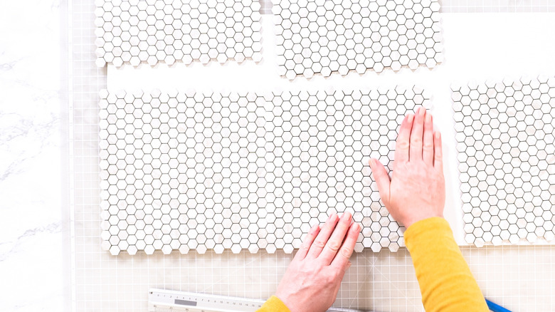 A person installing white peel-and-stick flooring