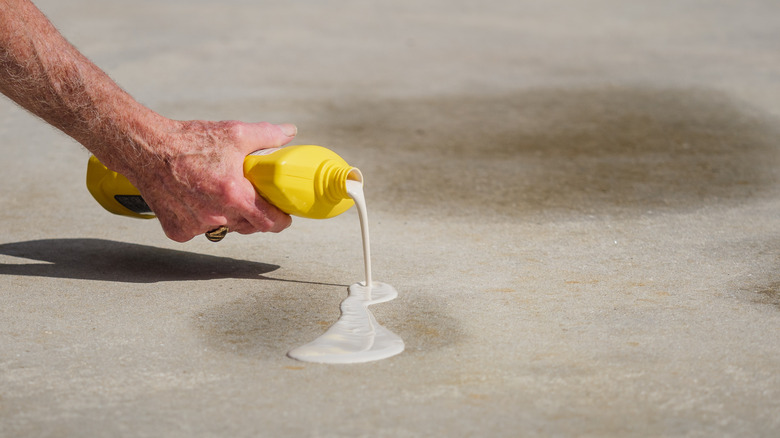 A person pouring an oil stain remover onto a driveway