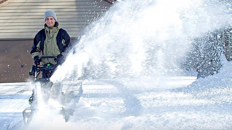 Man using an EGO snow thrower to clear a driveway