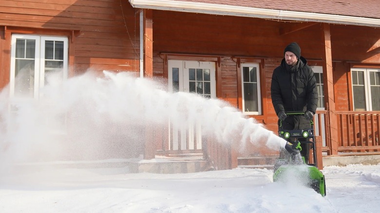 Person clearing a sidewalk of snow with a Greenworks snow thrower