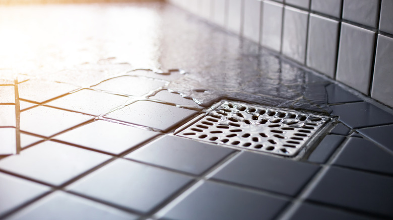 A drain in a tiled showerwith water in the background