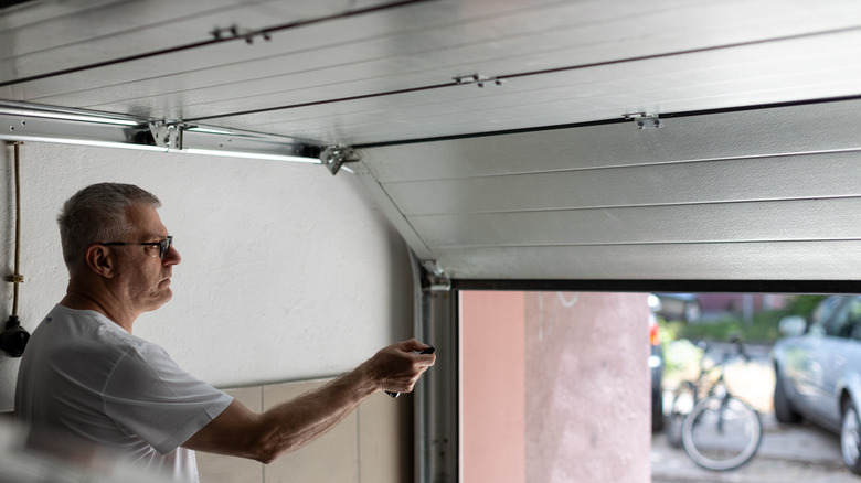 Old man wearing glasses opening garage door with remote controller