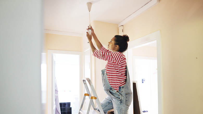 A woman standing on a ladder to change a light bulb